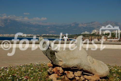 Türkei, Antalya, Türkische Riviera, Aussicht von Parkanlage mit Hand-Steinskulptur in der Altstadt beim Hafen zum Konyaalti-Strand mit Sicht auf die Berge. Personen, Sehenswürdigkeit. Turkey, Antalya-city,view from the park in the old town near the harbour with view along the coast-line with the mountains, ocean, Konyaalti-beach, people