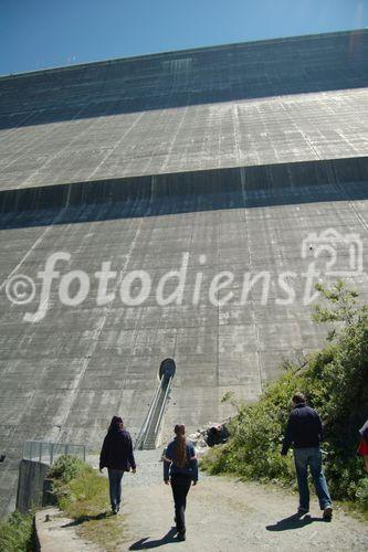 Winzig klein sind die Personen im Vergleich zur 285 Meter hohen Staumauer Grande Dixence. Small like anses are the people entering the 285 meters high wall of the water power station Grande Dixence in the valley of Hérenses. 
35 Gletscher speisen den Stausee Grande Dixence und die in Elektrizität umgewandelte Wasserkraft versorgt 400'000 Haushalte ein Jahr lang. 35 glaciers are delivering the melting water to the Lake Grande Dixence. The electricity that can be produced with the water power 
is suppling 400’000 houses per year with green electricity

Das Schmelzwasser von 35 Gletschern wird in der weltweit grössten Gewichtsstaumauer Grande Dixence im Wallis gespeichert und zu Strom für 400'000 Haushalte pro Jahr verarbeitet. Die 285 Meter hohe und an der Krone 700 Meter lange sowie am Sockel 200 Meter breite Staumauer vermag dem Druck von 400 Mio. m3 zu wiederstehen. Das Bauwerk
ist 15 Mio. Tonnen schwer, 6 Mio. Tonnen Beton wurden für den Bau verwendet. 
