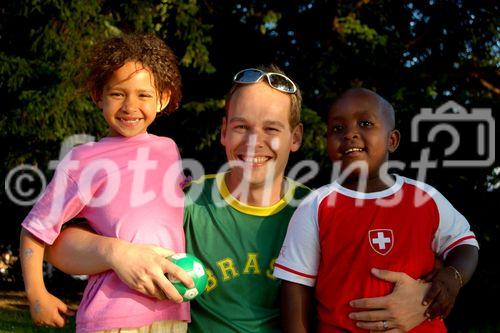 Ein junger Schweizer MAnn mit brasilianischem T-Shirt posiert mit einem jamaicanischen Mädchen und einem brasilianischen Einwanderer-Junge beim Fussball am Zürichseeufer. Integration fängt früh an und setzt die Bereitschaft der Schweizer Bevölkerung zur Annäherung an die Ausländer voraus