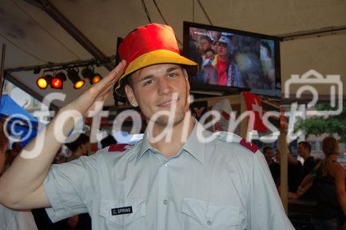 Schweizer Soldat mit deutschem Fanhut und in den NAtionalfarben Deutschands geschminktem Gesicht in Achtungsstellung in der Fanzone von Zürich. Swiss soldier with german hut and painted face with national colours of germany  in Zürich's Fanzone