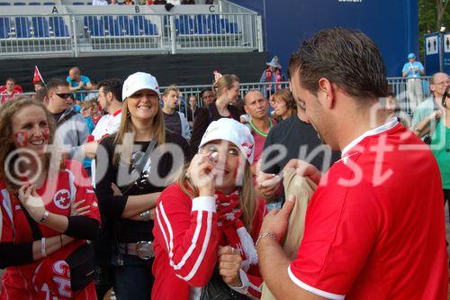 Weiblicher Fussballfan will Mann beim Fussballmatsch schminken und Frabe in sein Gesicht bringen. Female footballfan tries to put a make up on the mans face