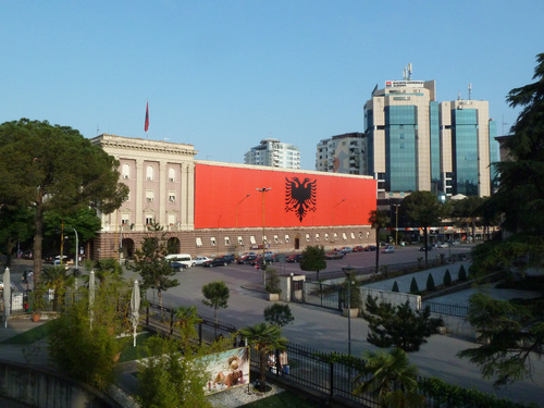 Zwanzig Jahre nach dem politischen Umbruch sucht Albanien Anschluss an Europa. Rechts- und Politikstrukturen sind auf dem Weg, die Wirtschaft boomt dank dem immensen Nachholbedarf beim Bauen und Konsumieren. Albaniens Hauptstadt Tirana ist in nur einer Generation von 100.000 auf über 500.000 Einwohner gewachsen. Im Bild: Die große Flagge auf dem Regierungsgebäude ist noch von der 100-Jahr-Feier der Unabhängigkeit Albaniens übrig geblieben.