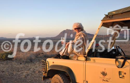 Genus pur in der Wildnis. Eine Touristin geniesst den Sonnenuntergang im Samburu Nationalpark mit einem Glass Champagner. Enjoying a sundowner champagne glass in the wilderness of Samburu Nationalpark 