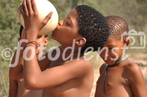 Ein Mädchen einer Naro-San Bushmen Gruppe trinkt aus dem Straussenei, dass zuvor im Wüstenboden der Kalahari vergraben war