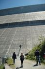 Winzig klein sind die Personen im Vergleich zur 285 Meter hohen Staumauer Grande Dixence. Small like anses are the people entering the 285 meters high wall of the water power station Grande Dixence in the valley of Hérenses. 35 Gletscher speisen den Stausee Grande Dixence und die in Elektrizität umgewandelte Wasserkraft versorgt 400'000 Haushalte ein Jahr lang. 35 glaciers are delivering the melting water to the Lake Grande Dixence. The electricity that can be produced with the water power is suppling 400’000 houses per year with green electricityDas Schmelzwasser von 35 Gletschern wird in der weltweit grössten Gewichtsstaumauer Grande Dixence im Wallis gespeichert und zu Strom für 400'000 Haushalte pro Jahr verarbeitet. Die 285 Meter hohe und an der Krone 700 Meter lange sowie am Sockel 200 Meter breite Staumauer vermag dem Druck von 400 Mio. m3 zu wiederstehen. Das Bauwerkist 15 Mio. Tonnen schwer, 6 Mio. Tonnen Beton wurden für den Bau verwendet. 