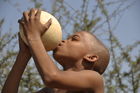 Ein junger Buschman trinkt Wasser aus einem Straussenei, dass im Boden der Kalahari-Wüste vergraben war