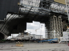 Die Nahbetrachung des New Safe Confinement zeigt die enorme größe des Gebäudes. Hier nicht zu sehen sind immense Stahlträger an der Decke der neuen Hülle, an denen Kräne befestigt werden sollen, die eines Tages den Rückbau des Reaktorgebäudes ermöglichen sollen. Das wird jedoch lange dauern. Der neue Sarkophag soll eine Lebensdauer von rund 100 Jahren haben.